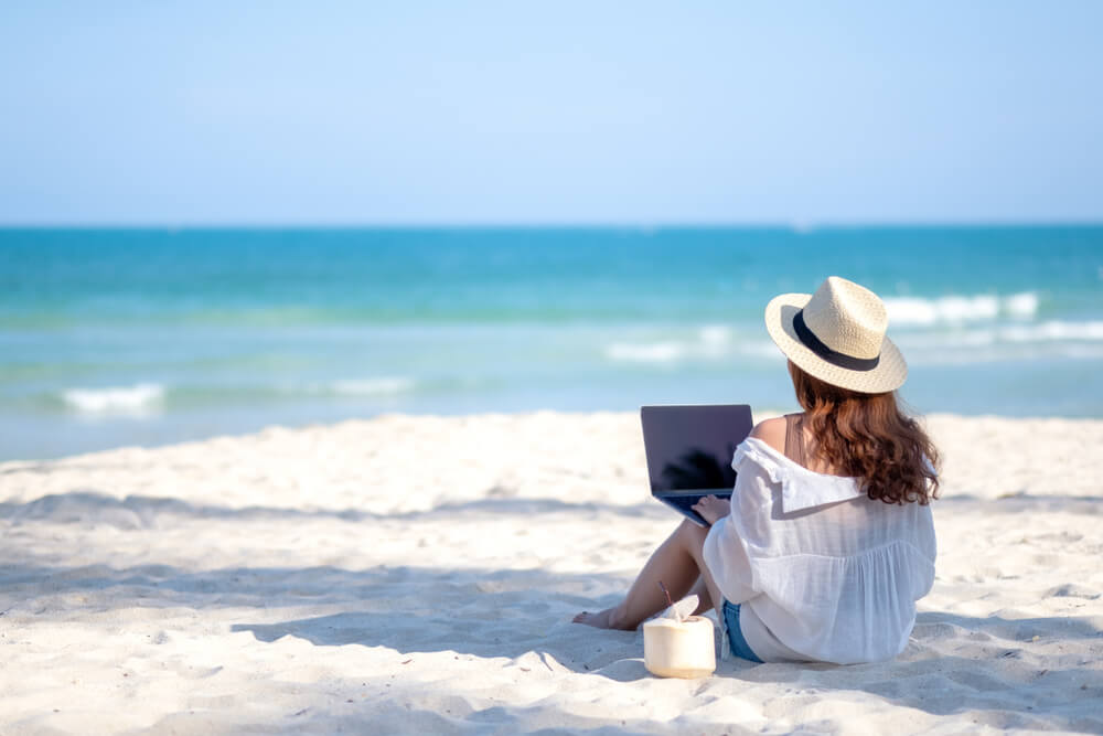 Person sitting on the beach and working on their laptop, long term rentals in Aruba for your workcation